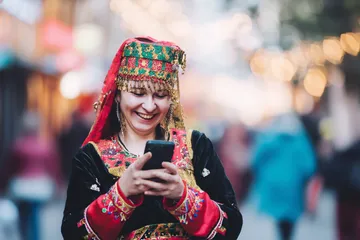 A cheerful woman in traditional clothing using her smartphone during a festive moment, showing how easily the TAS71 app fits into everyday life.